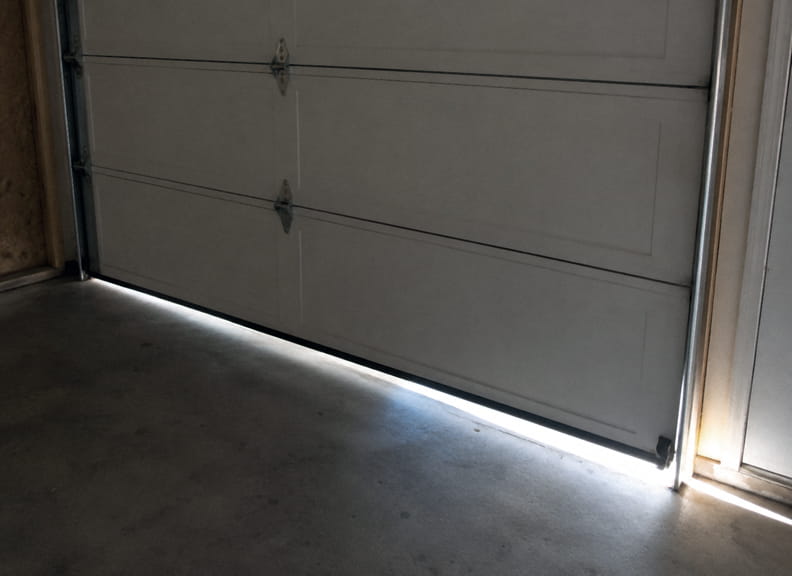Garage door sitting uneven with daylight visible under one corner, a common sign of a broken torsion spring.
